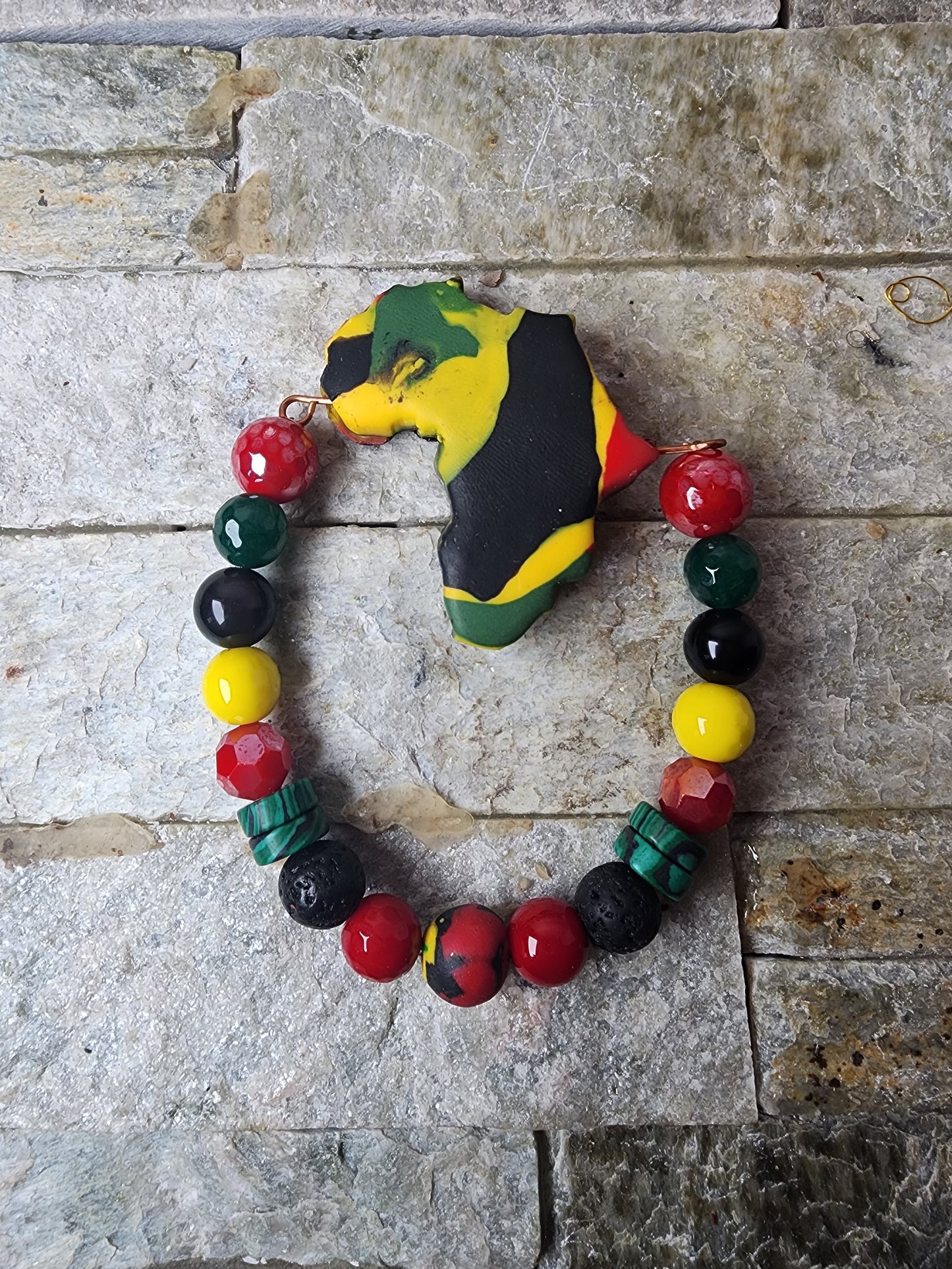 Handmade bracelet with polymer clay beads in Pan-African colors, spike shapes, jade gemstones, and a bold Africa-shaped focal bead — honoring heritage and spiritual power.