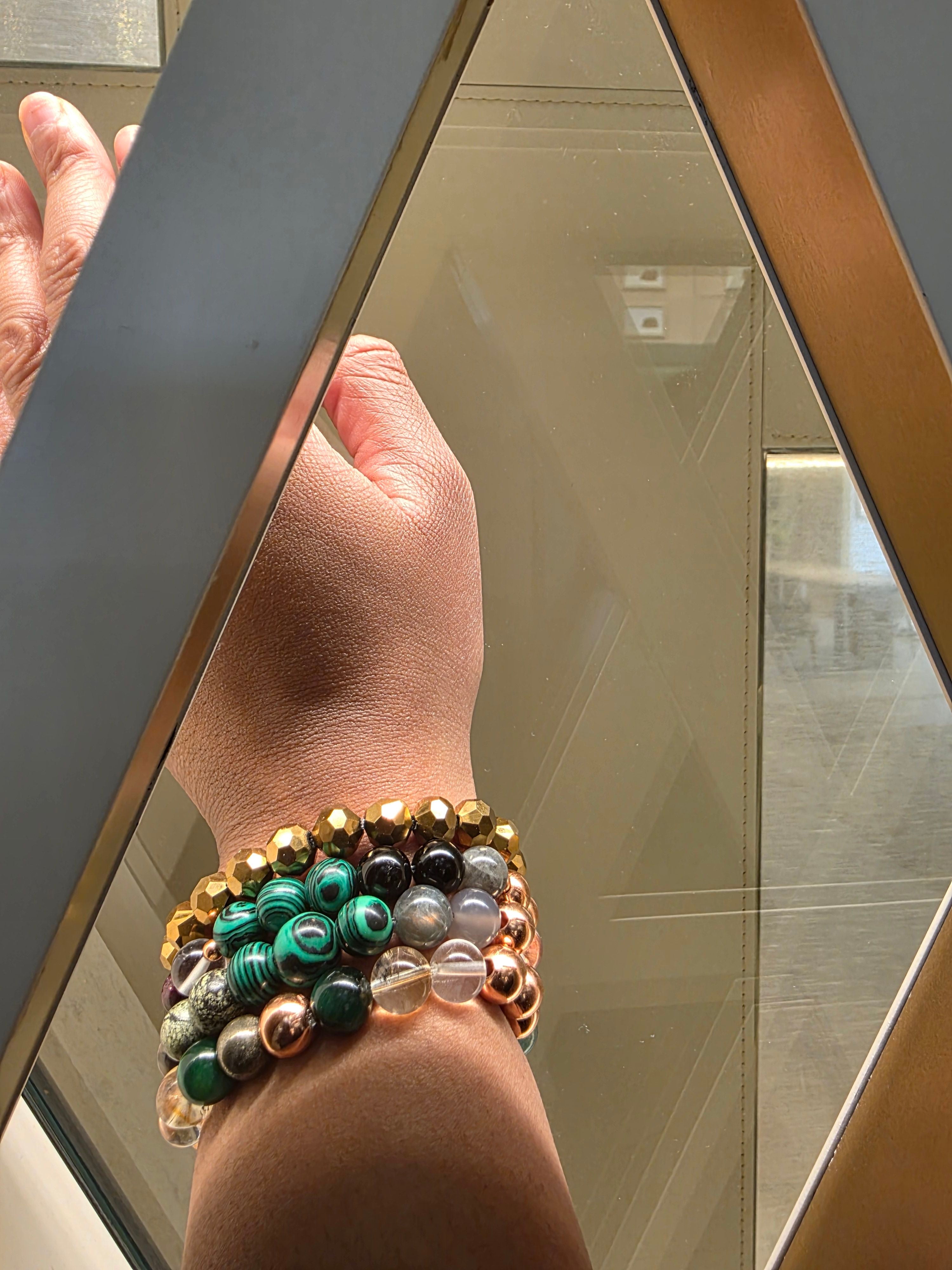 Jaz wearing a stacked set of golden, green malachite, and crystal bracelets by JvOR, glowing in natural light.”
