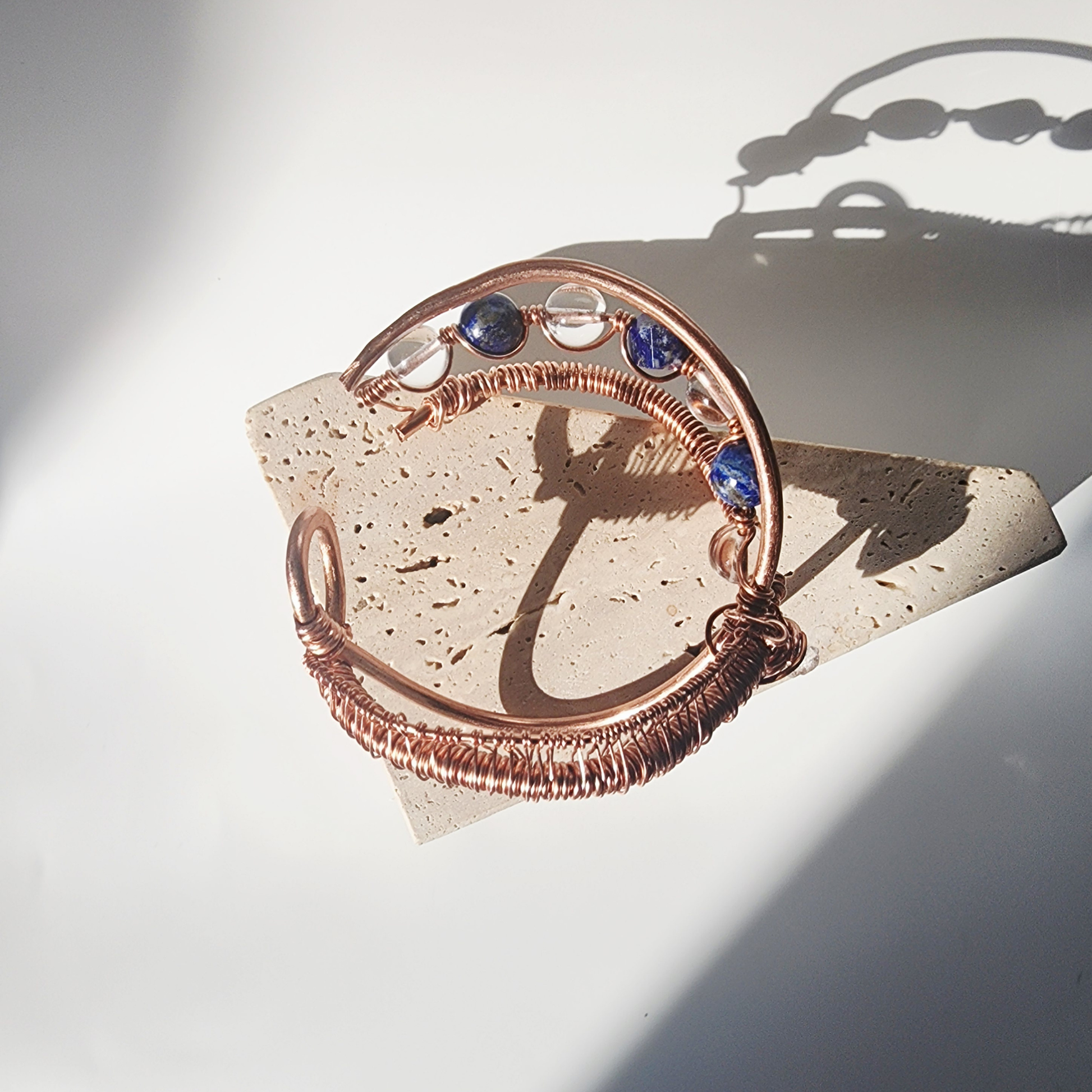 handmade copper cuff bracelet with herkimer diamond clear quartz and lapis lazuli crystals displayed on stone block
