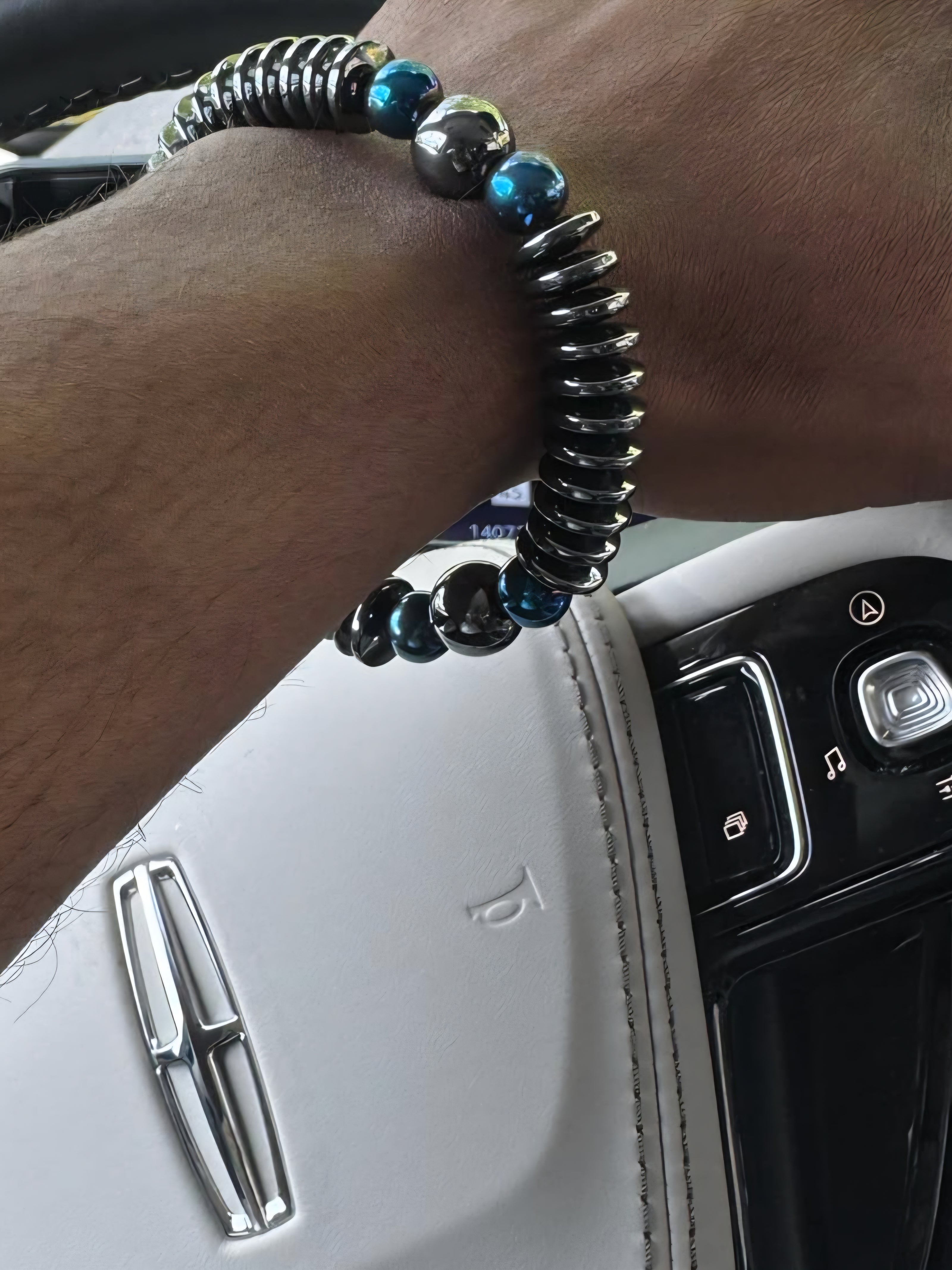 Empowerment Collection men’s hematite and blue crystal bracelet by JvOR, styled on the wrist while driving a Lincoln.”